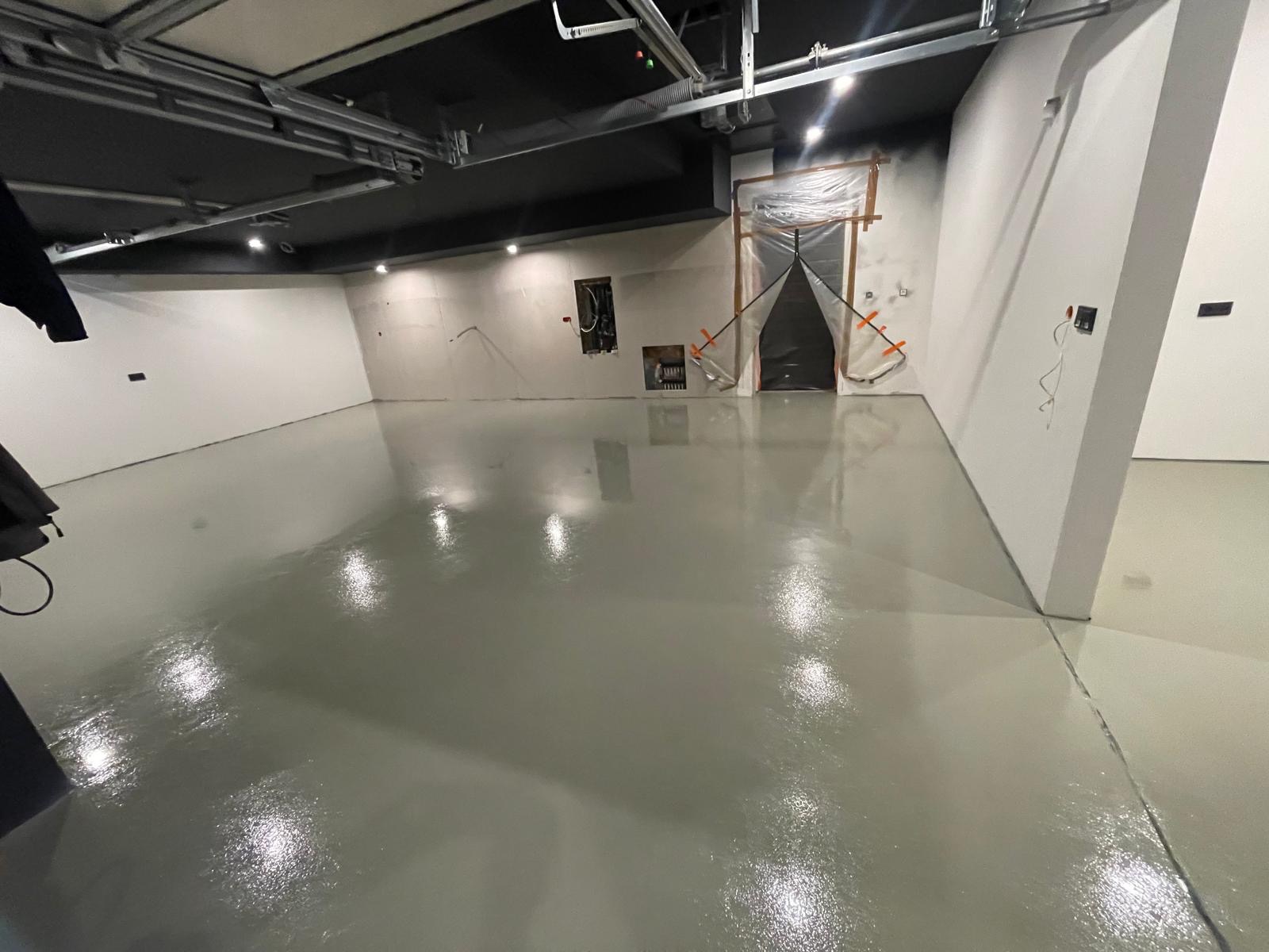 Świeżo wylana, jasnoszara posadzka z połyskiem w surowym wnętrzu, zabezpieczone wejście folią malarską.