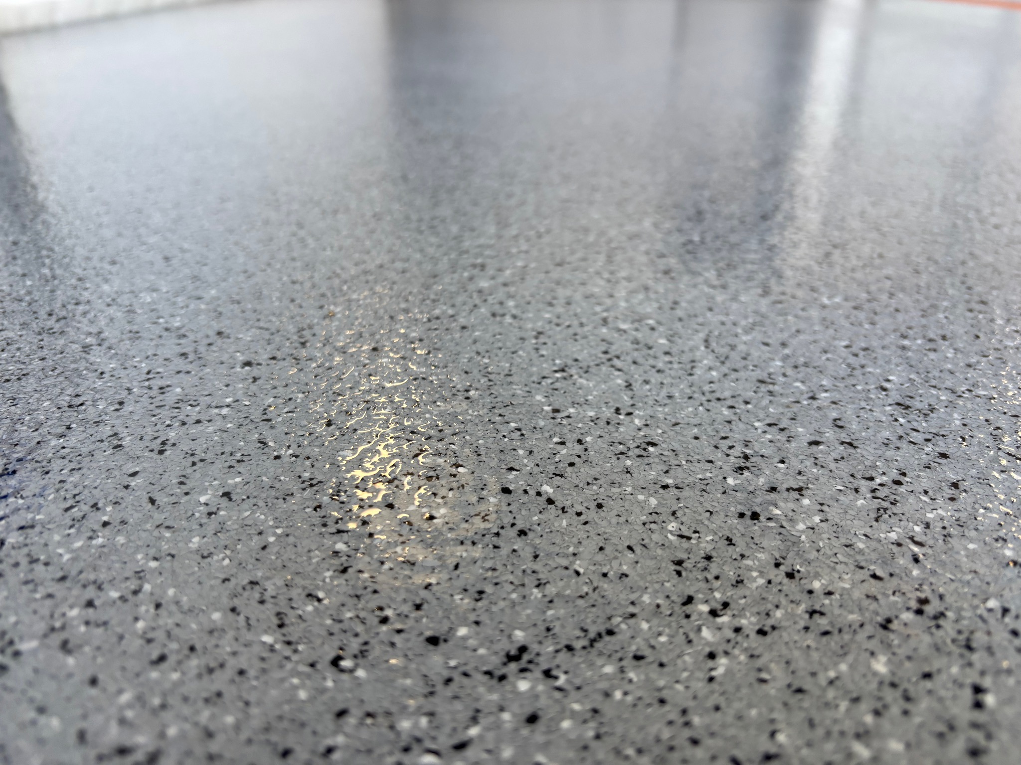 Szara posadzka żywiczna z czarnymi i białymi drobnymi kamyczkami, błyszcząca powierzchnia z refleksami światła, ujęcie z niskiej perspektywy.