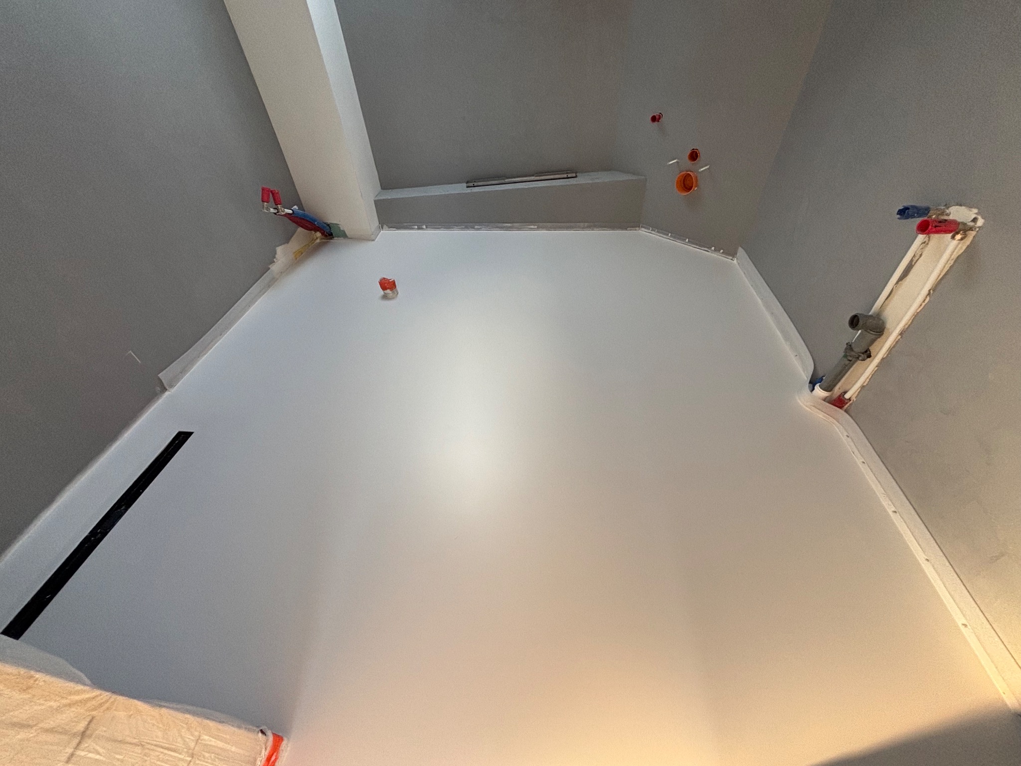 Świeżo wylana, jasnoszara podłoga w pomieszczeniu w trakcie remontu, widoczne wystające rury i instalacje na ścianach.