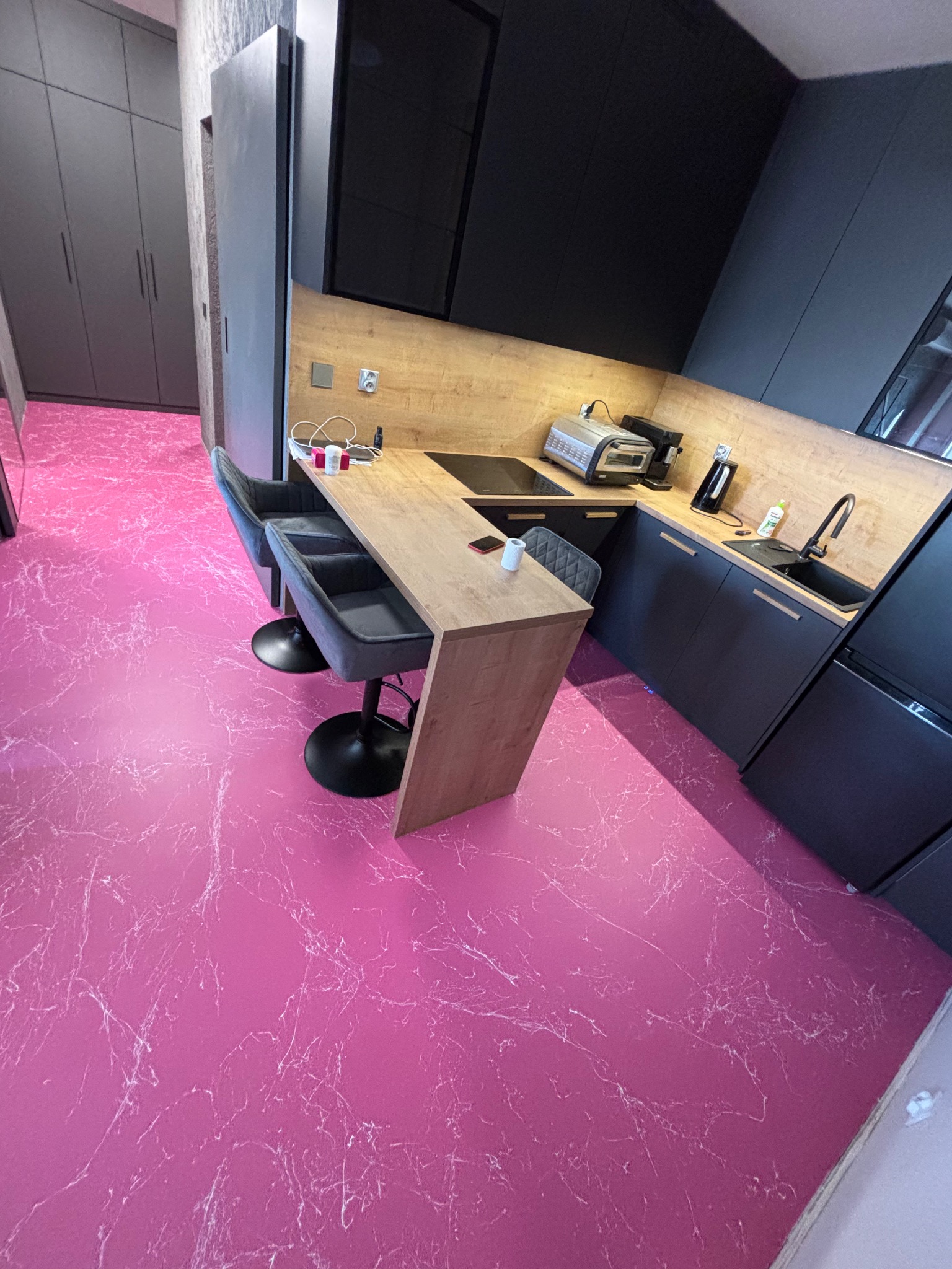 Żywiczna posadzka w odcieniu fuksji z białym marmurkowym wzorem w nowoczesnej kuchni z czarnymi szafkami i drewnianym blatem.