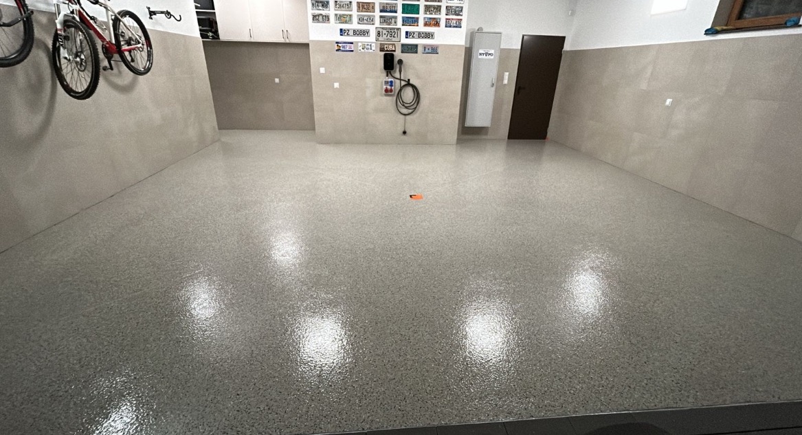 Gładka, szara posadzka w garażu z połyskiem, z rowerami na ścianie i dekoracyjnymi tablicami rejestracyjnymi. Widoczne drzwi i szafki.
