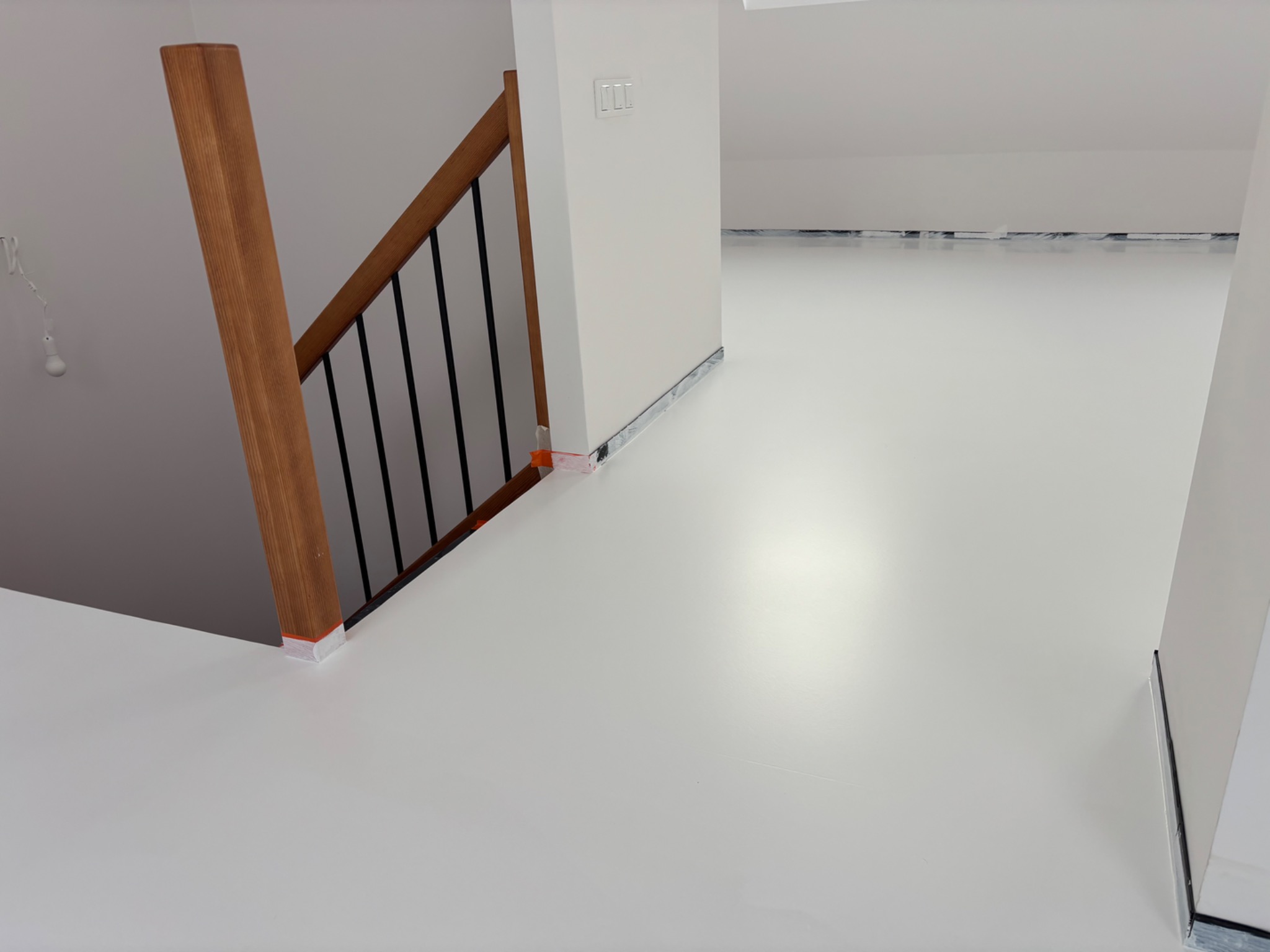 Jasna, jednolita posadzka w nowoczesnym wnętrzu z drewnianą balustradą schodów. Zabezpieczone listwy przypodłogowe. Minimalistyczny design, neutralna kolorystyka.