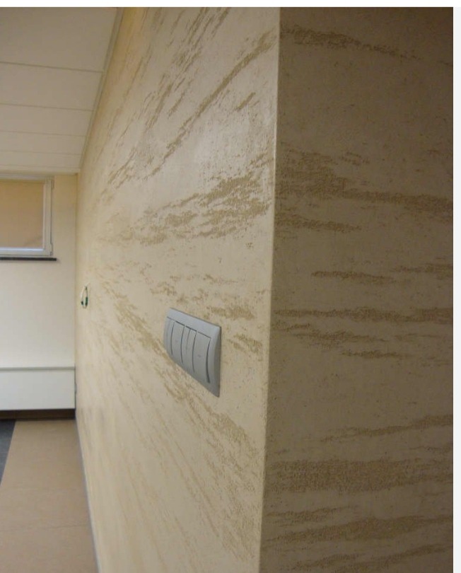 Ściana wewnętrzna z dekoracyjną, beżowo-piaskową fakturą, widoczny narożnik i włącznik światła z pięcioma przyciskami.