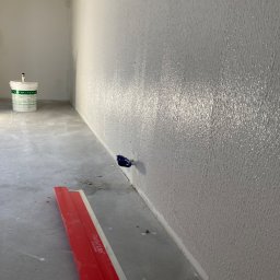 Sergiej Krykun - Świeżo nałożona, błyszcząca gładź na ścianie w rogu pomieszczenia, widoczna puszka z farbą i czerwona szpachla Parfait Liss na podłodze.