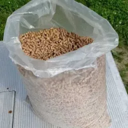 Wypełniony brązowawymi granulkami przezroczysty worek foliowy, częściowo otwarty, leżący na szarej, płaskiej powierzchni na tle trawy.