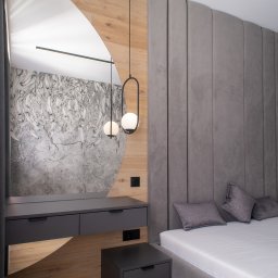 Patrycja Kucharek Studio10 - Nowoczesna sypialnia z szarą tapicerowaną ścianą, łóżkiem z szarą ramą i szafkami nocnymi w kolorze grafitowym, toaletka z lustrem o nietypowym kształcie oraz dekoracyjna lampa wisząca z dwoma...