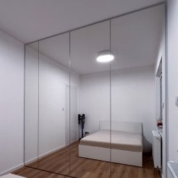 Patrycja Kucharek Studio10 - Nowoczesna szafa wnękowa z lustrzanymi drzwiami przesuwnymi, odbijająca wnętrze sypialni z łóżkiem i drewnianą podłogą.