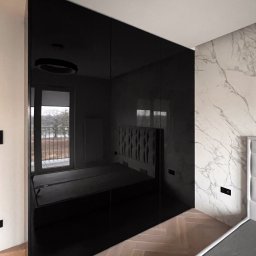 Patrycja Kucharek Studio10 - Czarna, błyszcząca zabudowa wnękowa z lustrzanymi drzwiami przesuwnymi, odbijająca wnętrze sypialni z łóżkiem i balkonem, na tle ściany z marmurowym wzorem i parkietem w jodełkę.