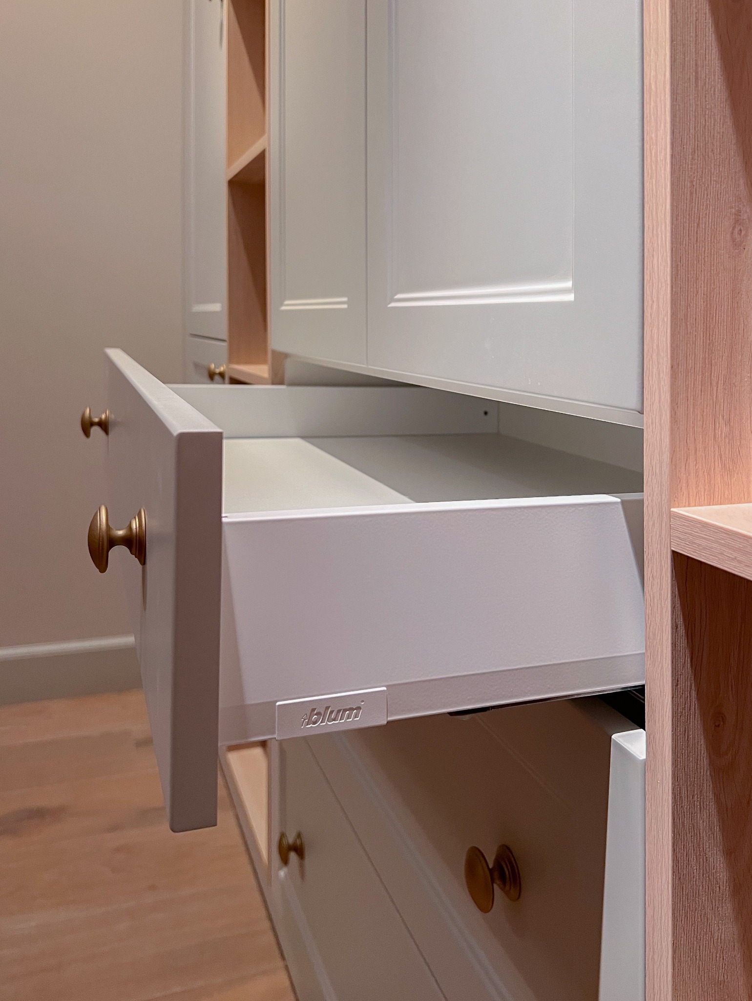 Otwarta szuflada w szafie na wymiar, z widocznym systemem Blum i złotymi gałkami, drewniana rama boczna.