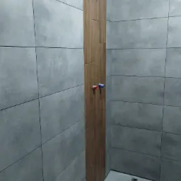 Szara, matowa, prostokątna okładzina ścienna z drewnopodobnym akcentem pionowym i wystającymi przyłączami wodnymi w narożniku łazienki.