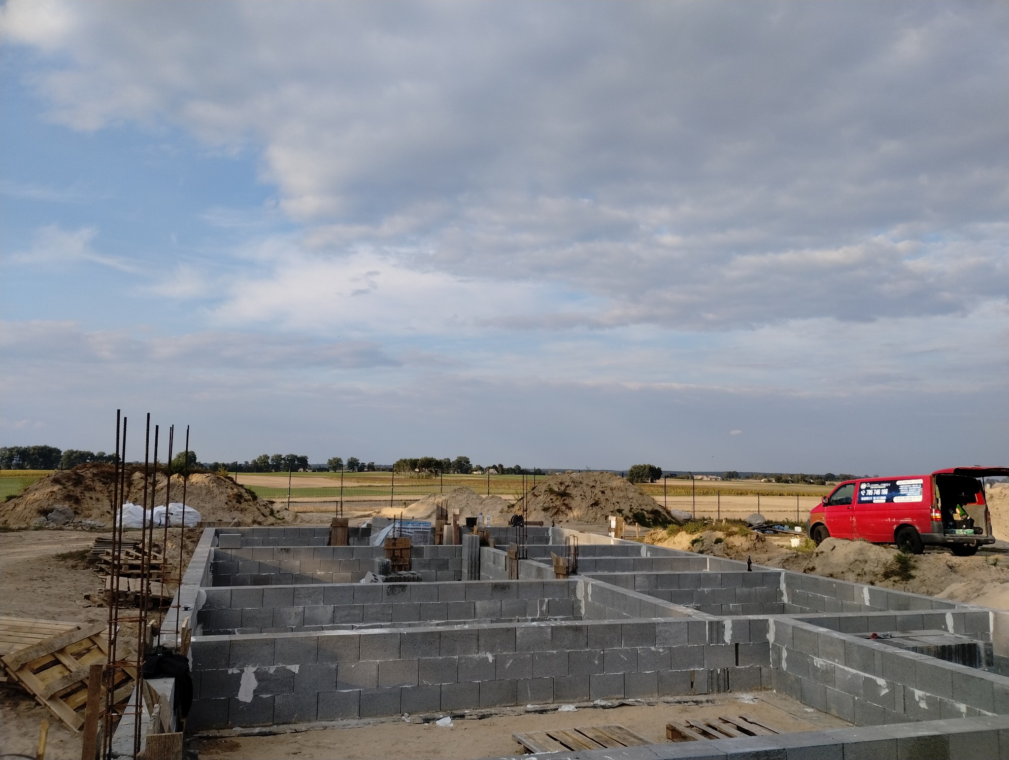 Fundamenty domu z bloczków betonowych na placu budowy, widoczny czerwony samochód dostawczy w tle.