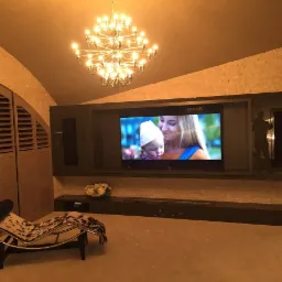 Salon z systemem audio-wideo zintegrowanym w zabudowie ściennej, oświetlenie punktowe i dekoracyjny żyrandol, fotel wypoczynkowy ze wzorem krowy.