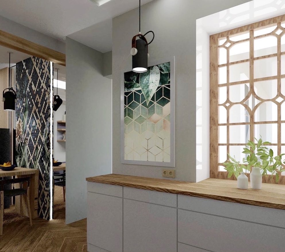 Nowoczesne wnętrze: białe szafki kuchenne z drewnianym blatem, geometryczny obraz z motywem roślinnym, dekoracyjne okno z drewnianą ramą i roślinami w wazonie, designerska lampa wisząca.
