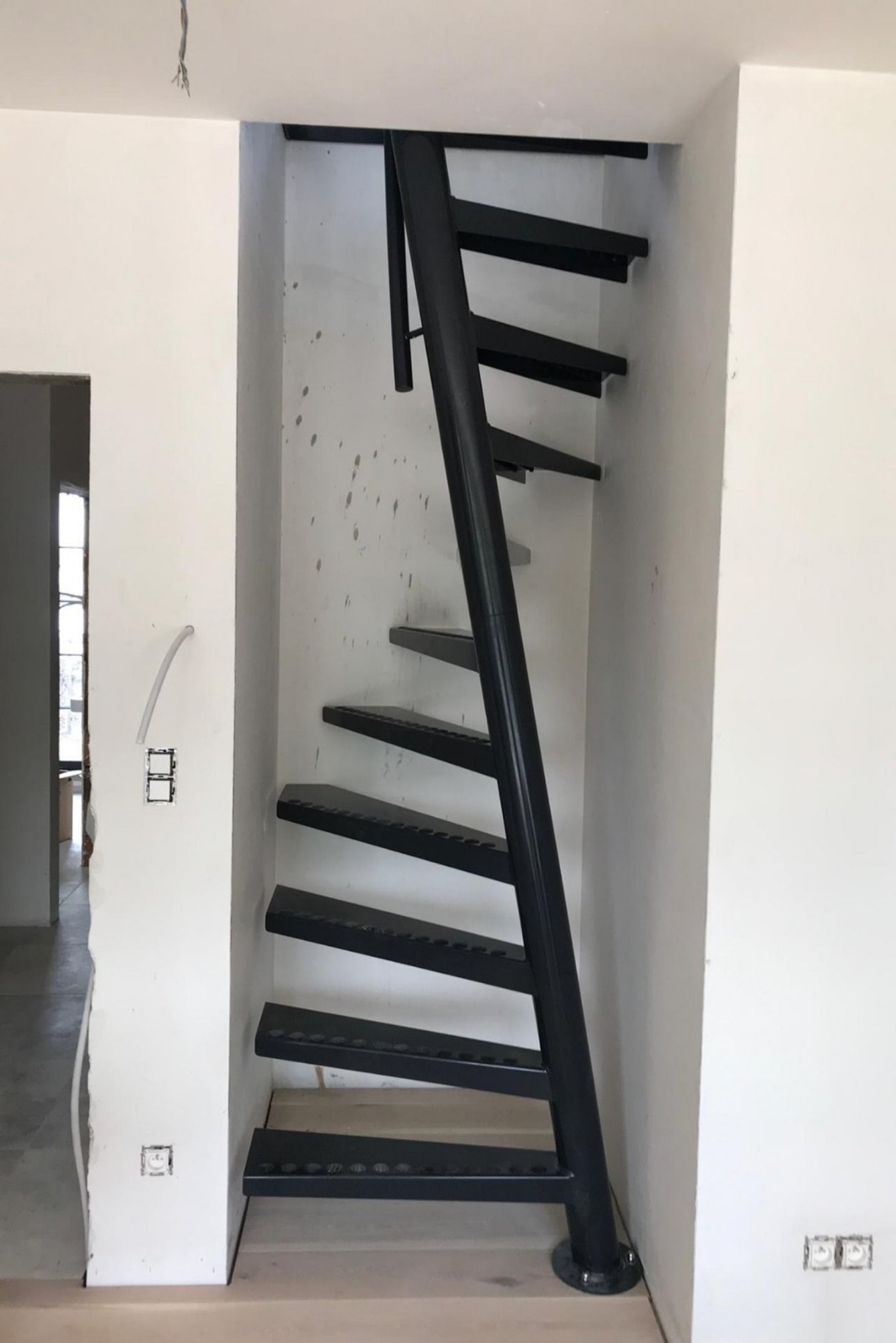 Metalowe schody spiralne w trakcie montażu w surowym wnętrzu, widoczne niedokończone ściany i instalacje elektryczne.