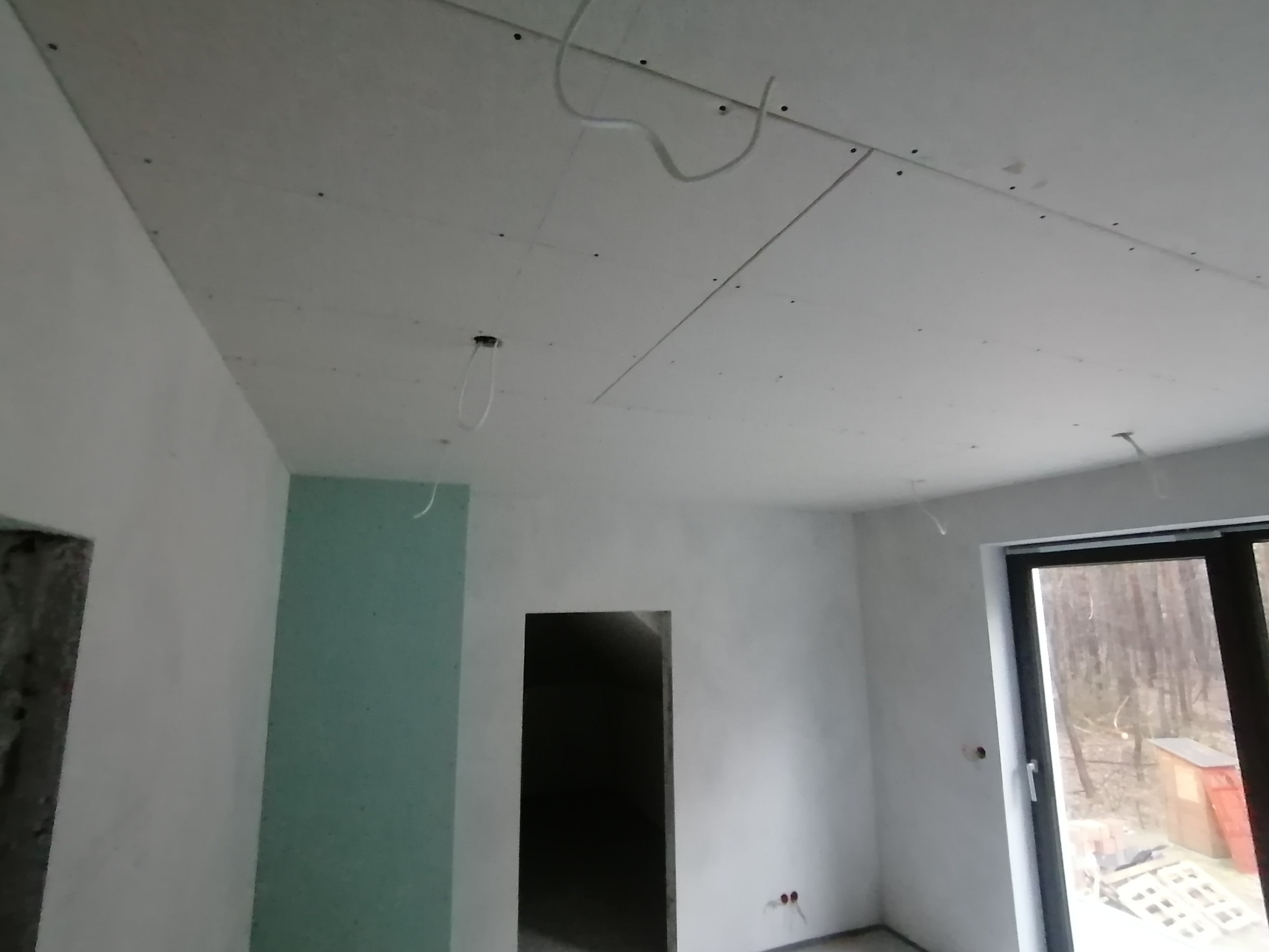 Montaż płyt kartonowo-gipsowych na suficie, widoczne przewody elektryczne i szpachlowane łączenia, surowy stan wykończenia wnętrza.