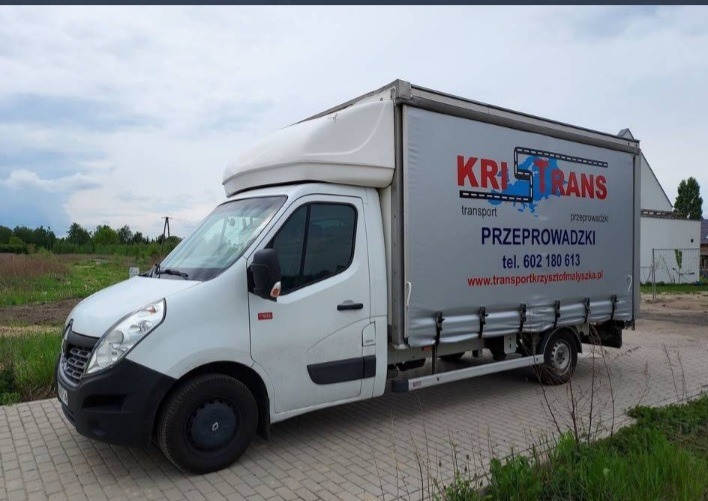 Biały samochód dostawczy Renault Master z nadrukiem logo firmy KRI-TRANS na plandece, zaparkowany na chodniku z kostki brukowej.