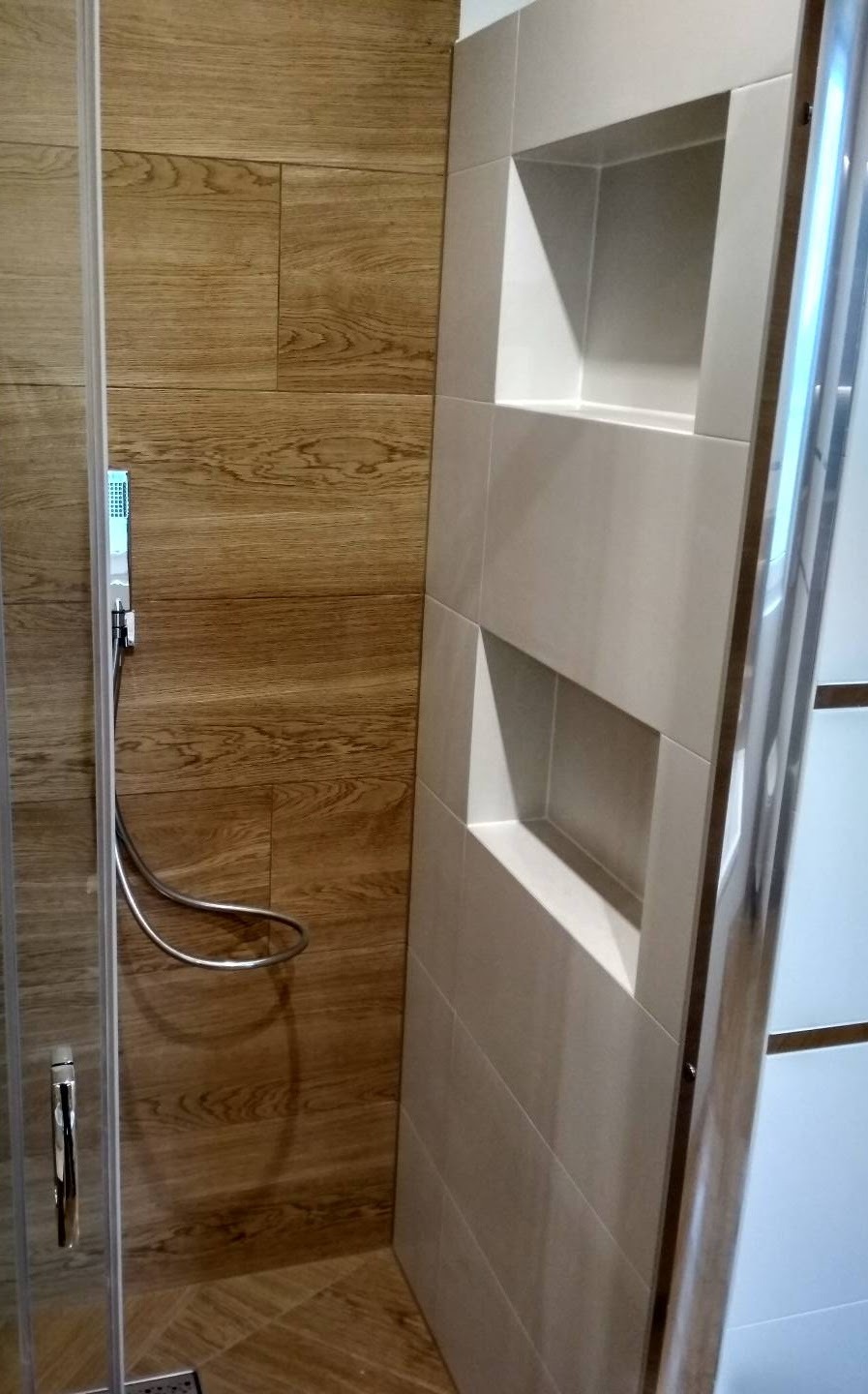 Nowoczesna kabina prysznicowa z drewnopodobnymi płytkami na ścianie i wnękami wykończonymi jasnymi płytkami.
