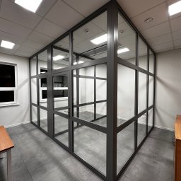 HoldCraft Sp. z o. o. - Szklana ścianka działowa z drzwiami w biurze, szara rama, widok z perspektywy, szare płytki podłogowe.