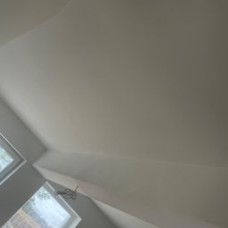 Kon-Stw Kompleksowe wykończenia wnętrz - Pomalowane na biało poddasze ze skośnym sufitem, widoczne dwa okna dachowe z białymi ramami oraz lampa sufitowa w stylu retro.