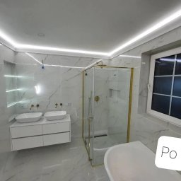 Kon-Stw Kompleksowe wykończenia wnętrz - Nowoczesna łazienka z marmurowymi płytkami, kabiną prysznicową ze złotymi ramami, podwójną umywalką na szafce z szufladami i oświetleniem LED pod sufitem.