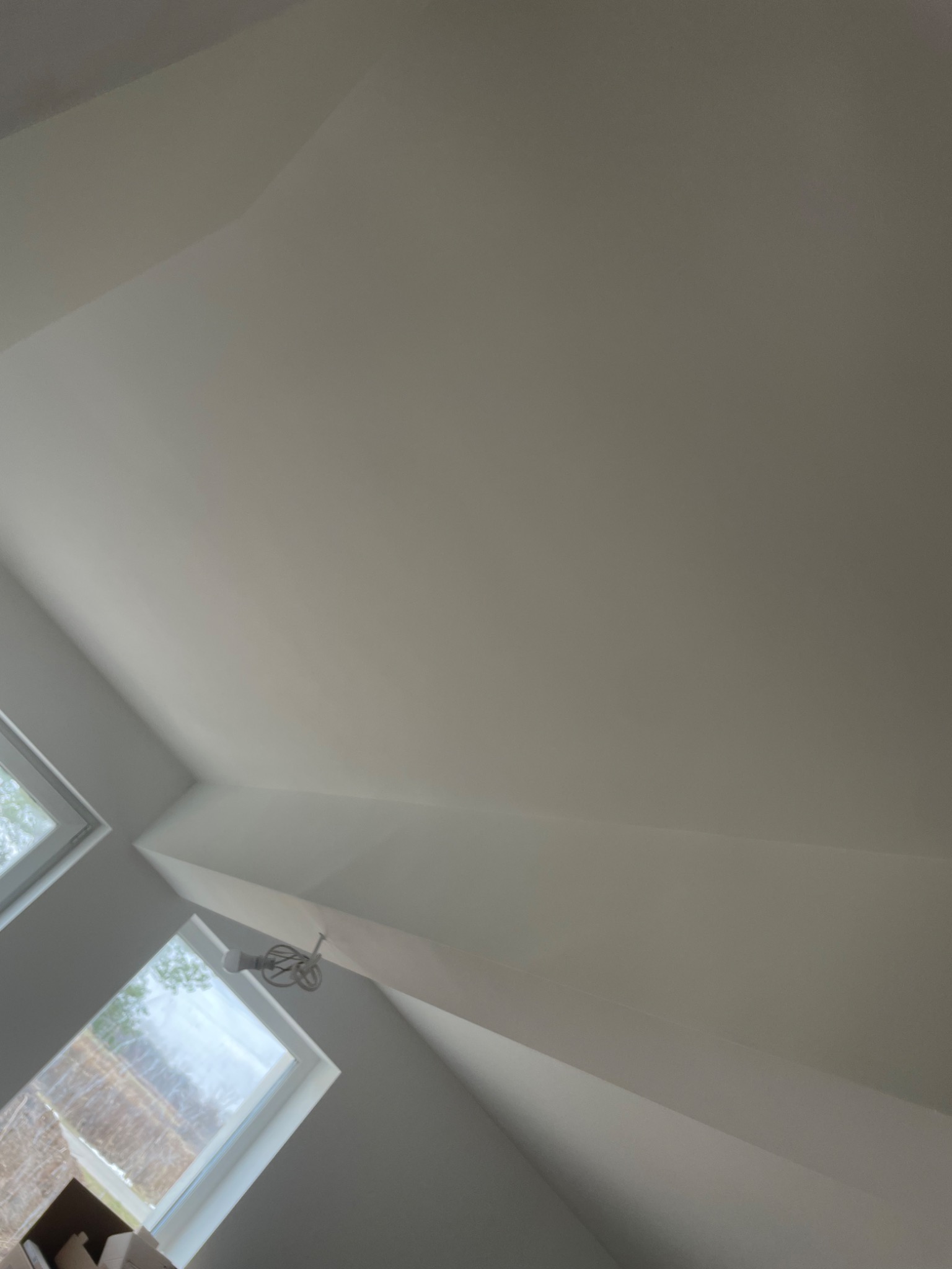 Pomalowane na biało poddasze ze skośnym sufitem, widoczne dwa okna dachowe z białymi ramami oraz lampa sufitowa w stylu retro.