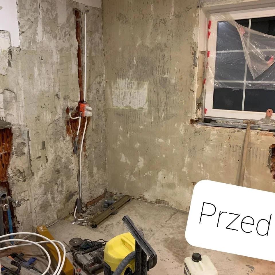 Zdjęcie łazienki w trakcie remontu: ściany częściowo pokryte szpachlą, widoczne instalacje, okno zabezpieczone folią, na podłodze narzędzia i odkurzacz przemysłowy, napis 'Przed'.