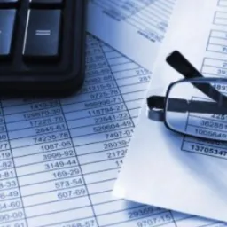 Kalkulator, okulary i wydrukowane zestawienie finansowe z rzędami liczb, stonowana kolorystyka.