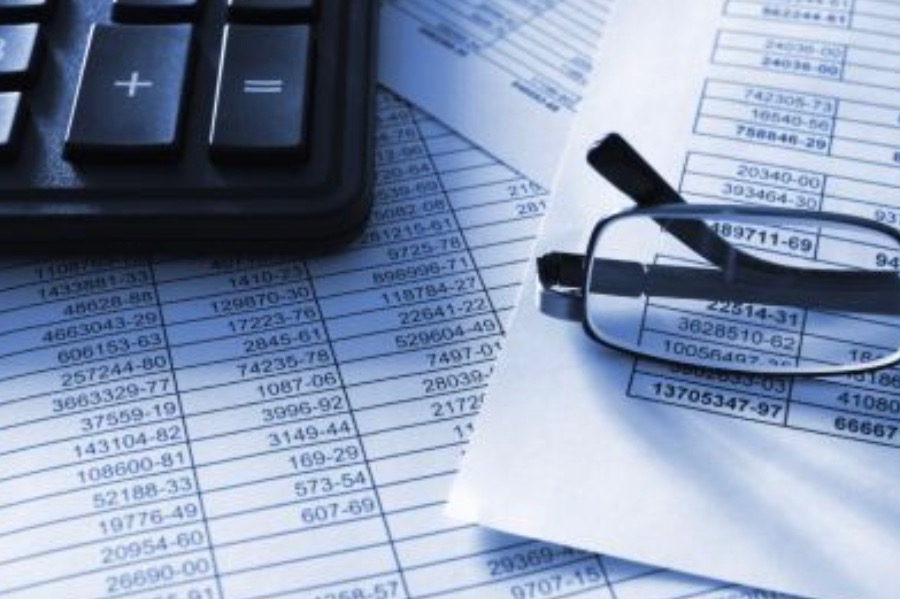 Kalkulator, okulary i wydrukowane zestawienie finansowe z rzędami liczb, stonowana kolorystyka.