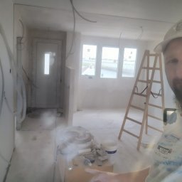 Perfectfinish - Wnętrze w trakcie prac wykończeniowych: widoczne przewody, drabina, okna i materiały budowlane. Ujęcie z perspektywy osoby wykonującej prace.