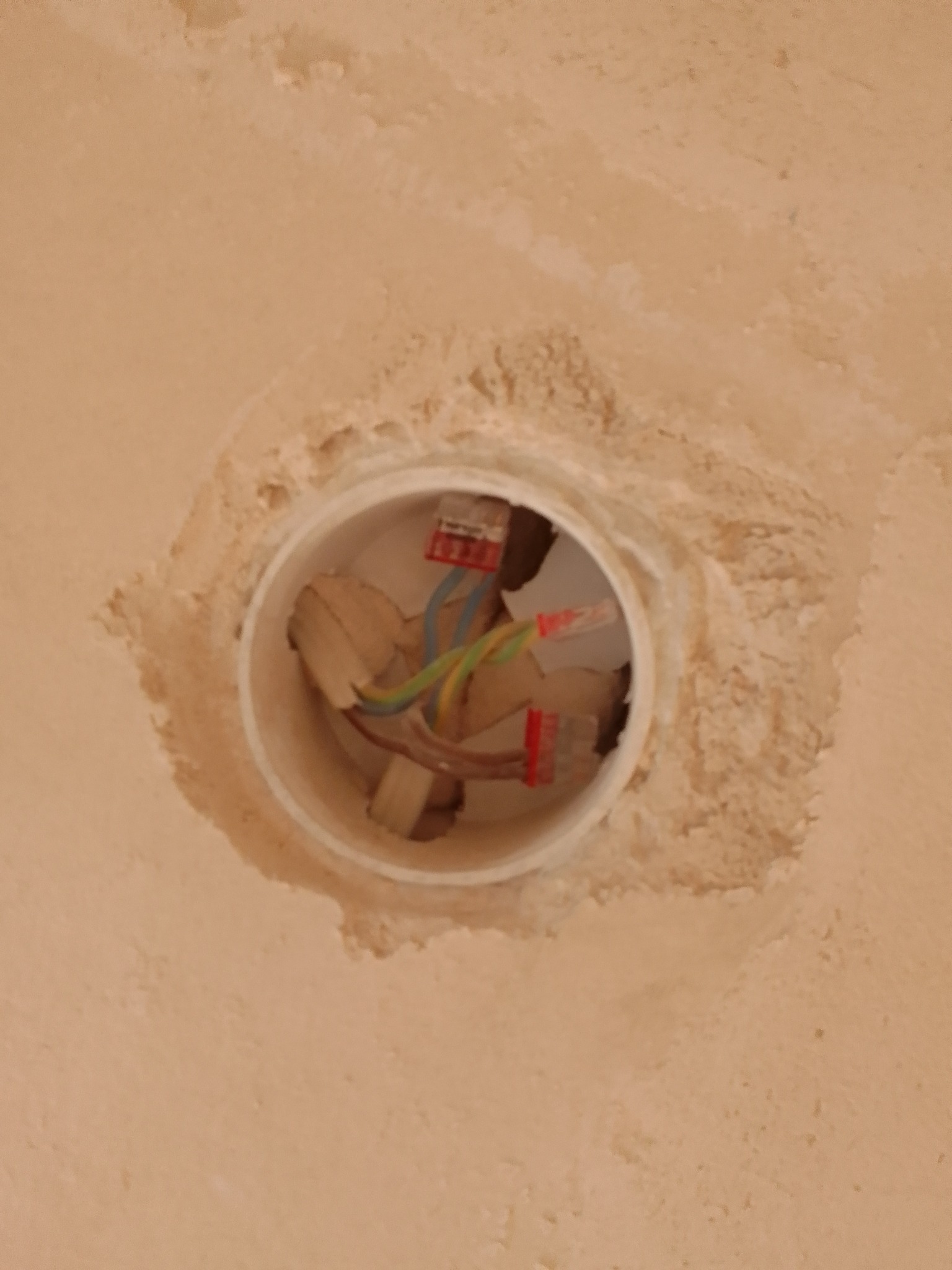 Otwór w ścianie z wystającymi przewodami elektrycznymi, złączki WAGO widoczne wewnątrz białej rury instalacyjnej, surowa powierzchnia ściany wokół otworu.