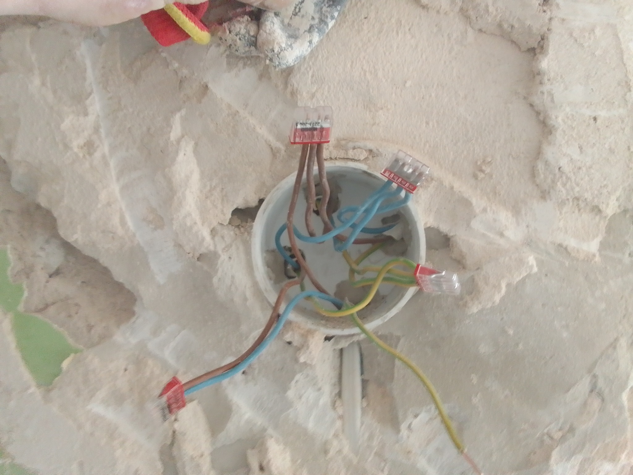 Otwór w ścianie z wystającymi przewodami elektrycznymi, połączonymi złączkami Wago, w trakcie prac remontowych.