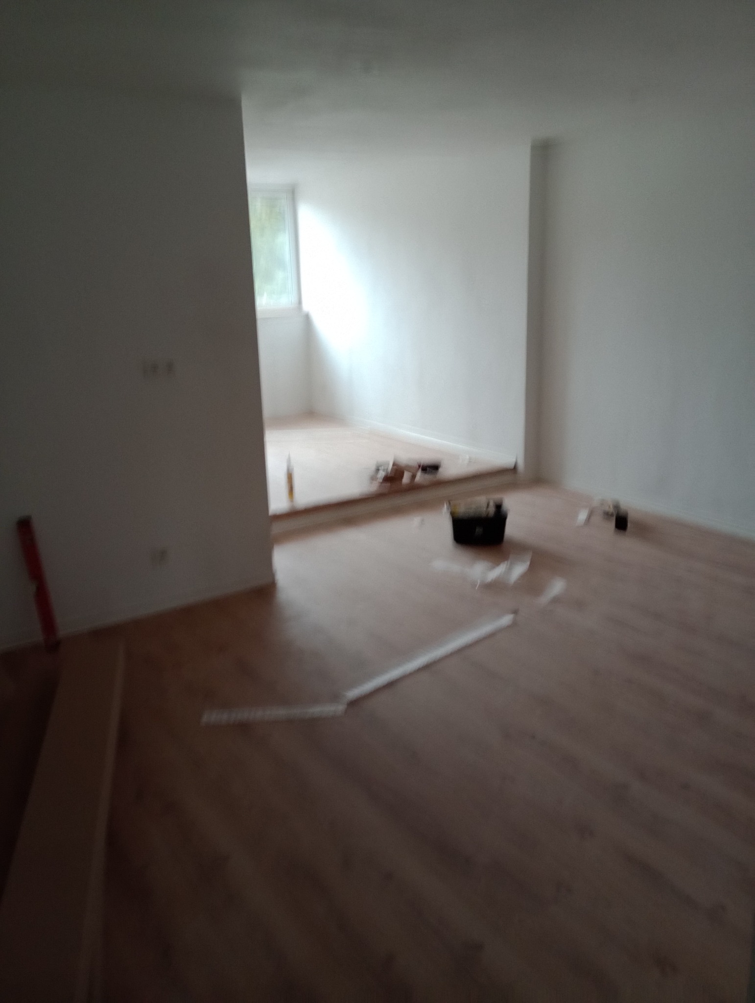 Ułożona podłoga z paneli w jasnym wnętrzu w Olsztynie. Widoczne narzędzia i akcesoria montażowe. Częściowo wykończone pomieszczenie z oknem.