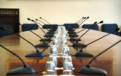 Stół konferencyjny z rzędem mikrofonów na giętkich ramionach i szklankami, przygotowany do spotkania.