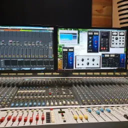 Profesjonalny stół mikserski w Garwolinie, z widocznymi dwoma monitorami prezentującymi oprogramowanie do edycji dźwięku, w tle panele akustyczne.