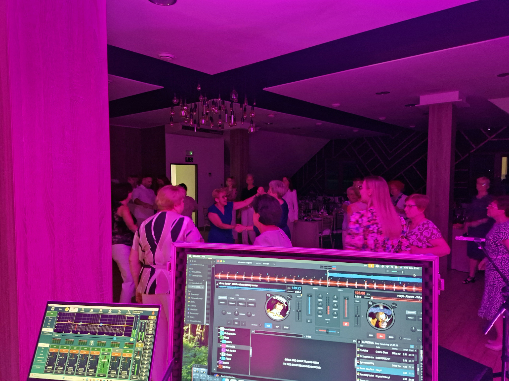 DJ gra muzykę na imprezie oświetlonej fioletowym światłem. Widoczny sprzęt DJ-ski i tańczący goście w tle. Atmosfera zabawy i rozrywki.