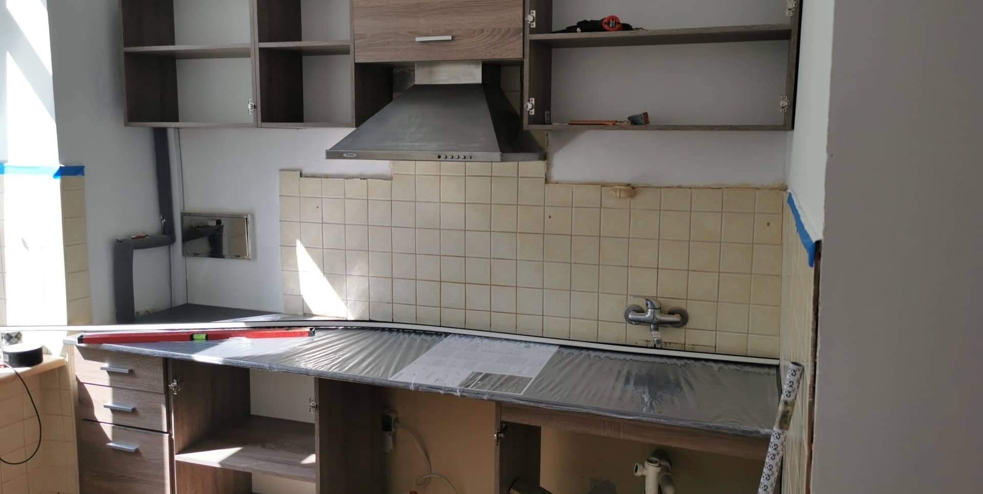 Kuchnia w trakcie remontu: częściowo zdemontowane stare płytki ścienne, zabezpieczony blat folią, widoczne narzędzia i poziomica.