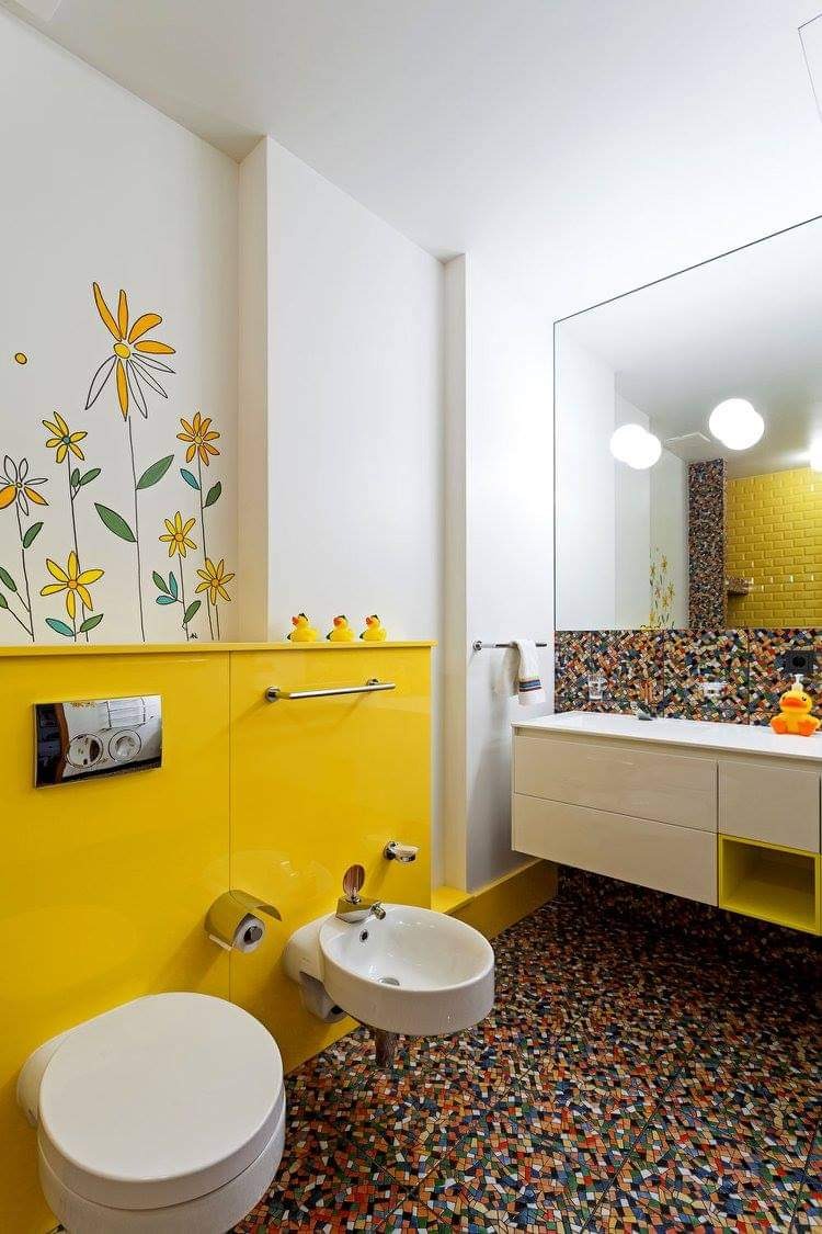 Żółto-biała łazienka z mozaikową podłogą, ozdobiona rysunkami kwiatów i gumowymi kaczuszkami, prezentuje nowoczesny design z wiszącą toaletą i bidetem.