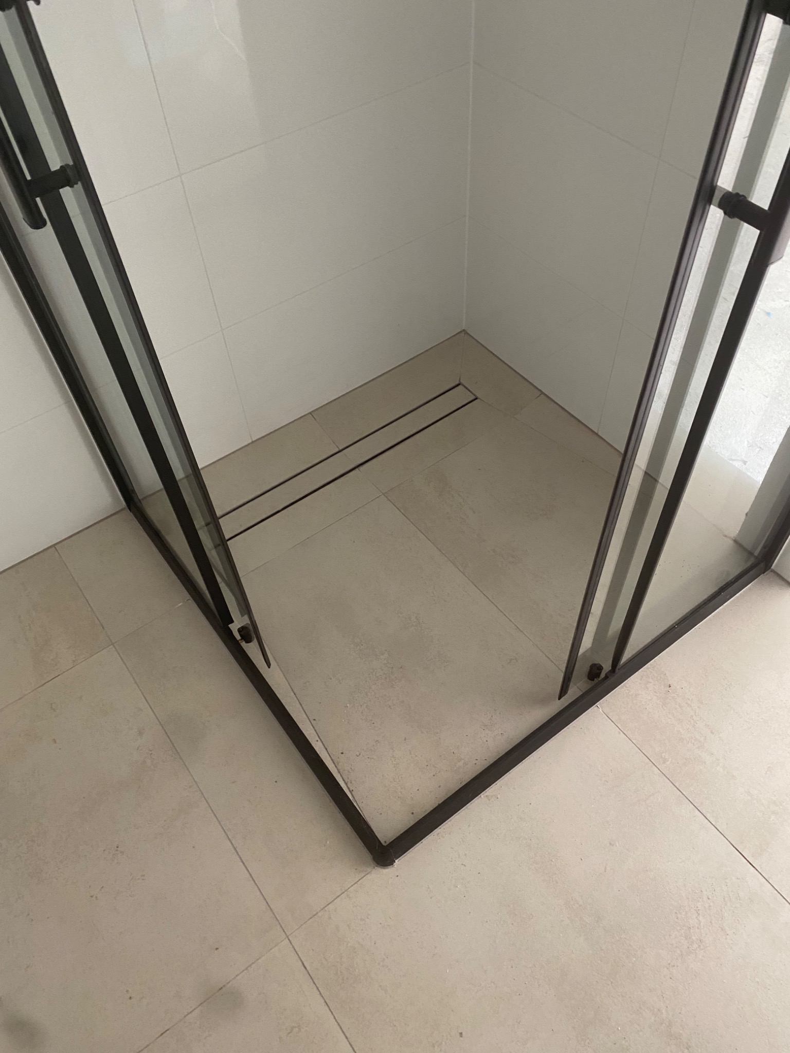 Kabina prysznicowa z czarnymi profilami i odpływem liniowym w rogu, wyłożona jasnymi, kwadratowymi płytkami na ścianach i podłodze.