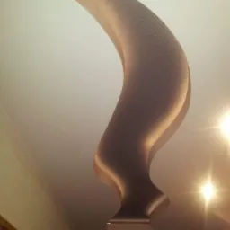 Dekoracyjny element gipsowy w kształcie rogu na suficie, oświetlony ciepłym światłem, widoczny fragment ściany i drzwi.