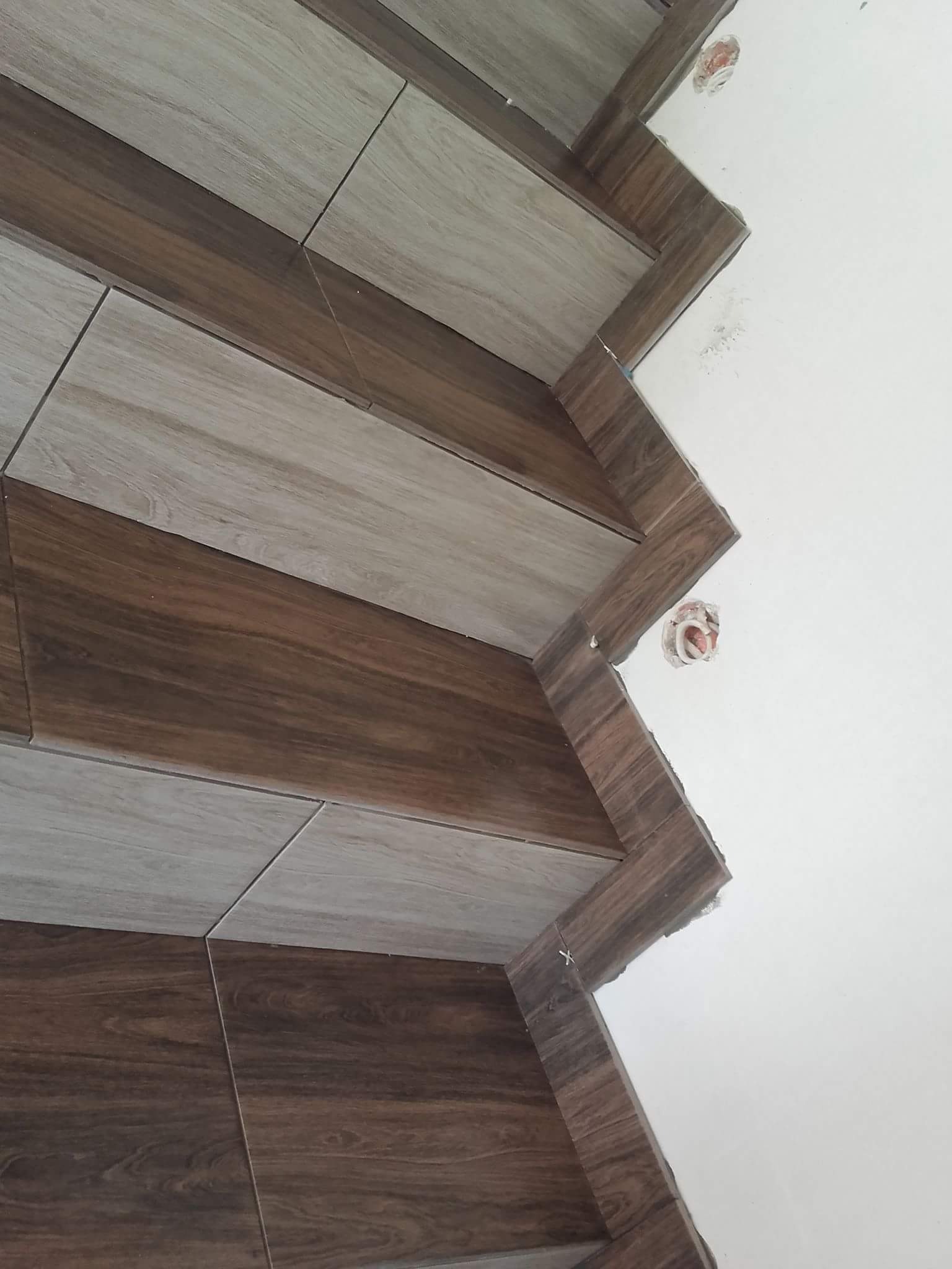 Ułożone płytki imitujące drewno w dwóch odcieniach brązu na ścianie, widoczny fragment instalacji elektrycznej.