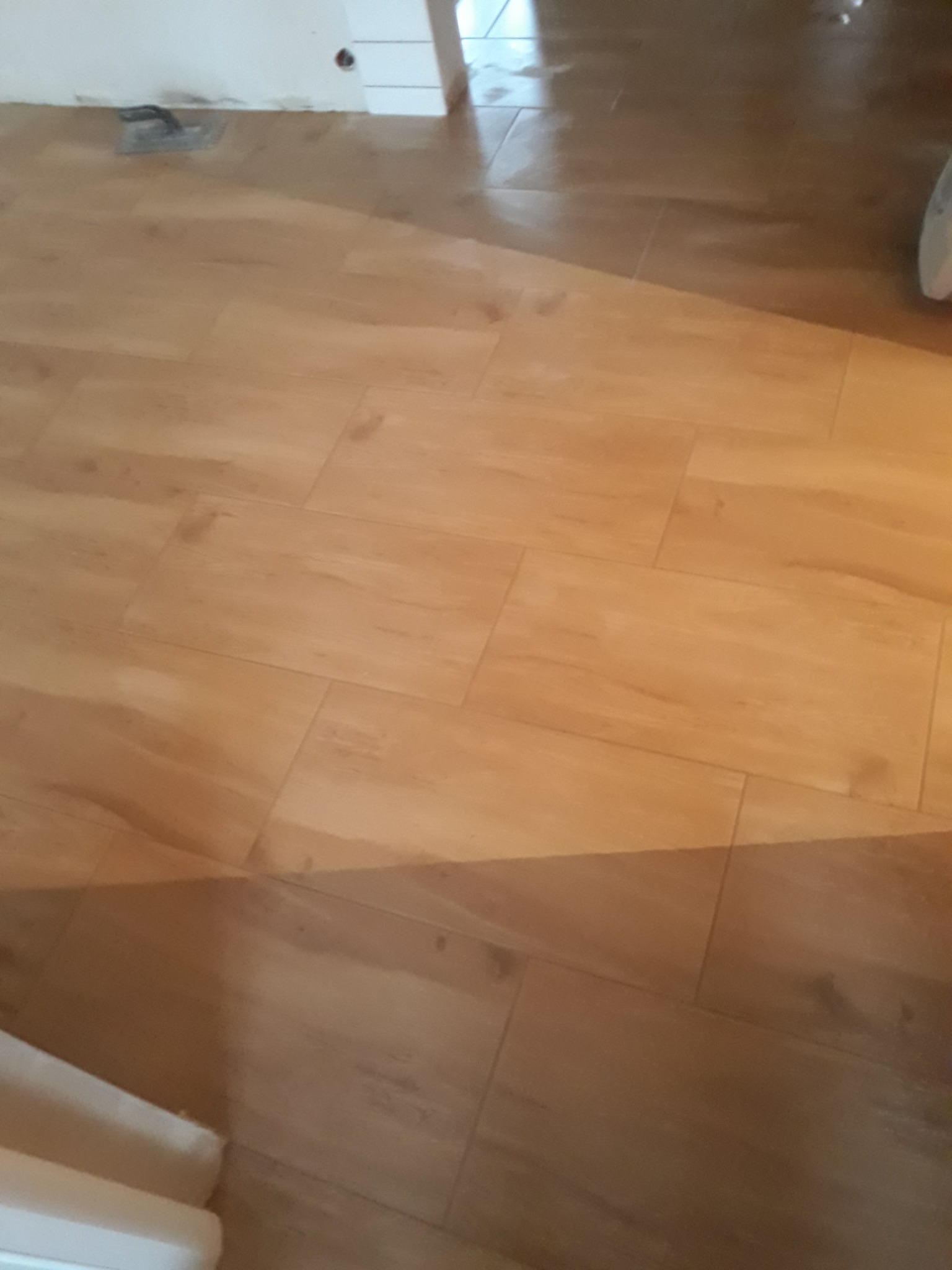 Ułożone panele podłogowe imitujące drewno, widoczna szpachelka przy progu, świeżo po ułożeniu.