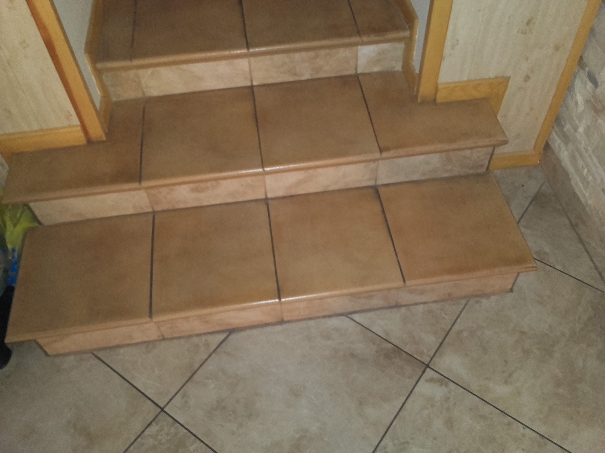 Wyłożone płytkami schody wewnętrzne z beżowych płytek, widoczne fugi i wykończenie drewniane na ścianach.