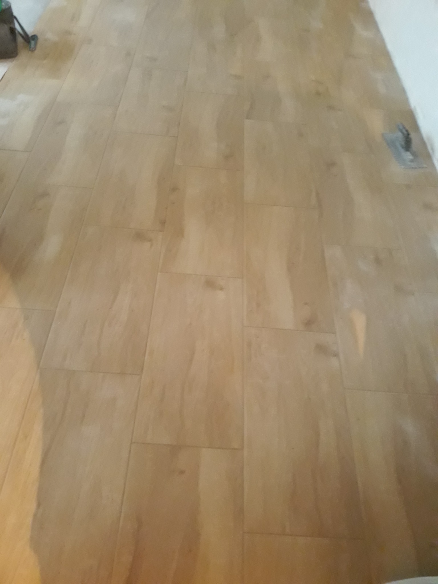 Ułożona podłoga z paneli imitujących drewno, widoczna paca glazurnicza przy ścianie, prawdopodobnie w trakcie prac wykończeniowych.