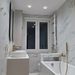 SEMI-BUD Serhii Semko - Elegancka łazienka w bieli i szarości z marmurowym wzorem, złote akcenty armatury, nowoczesne oświetlenie punktowe i grzejnik drabinkowy.