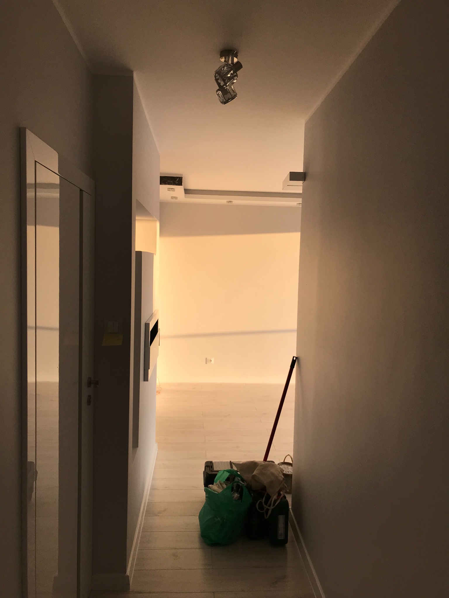 Korytarz w trakcie odświeżania: świeżo pomalowane szare ściany, odnowiona podłoga z jasnych paneli, widoczne akcesoria malarskie w rogu, w głębi pokój z oświetleniem sufitowym.