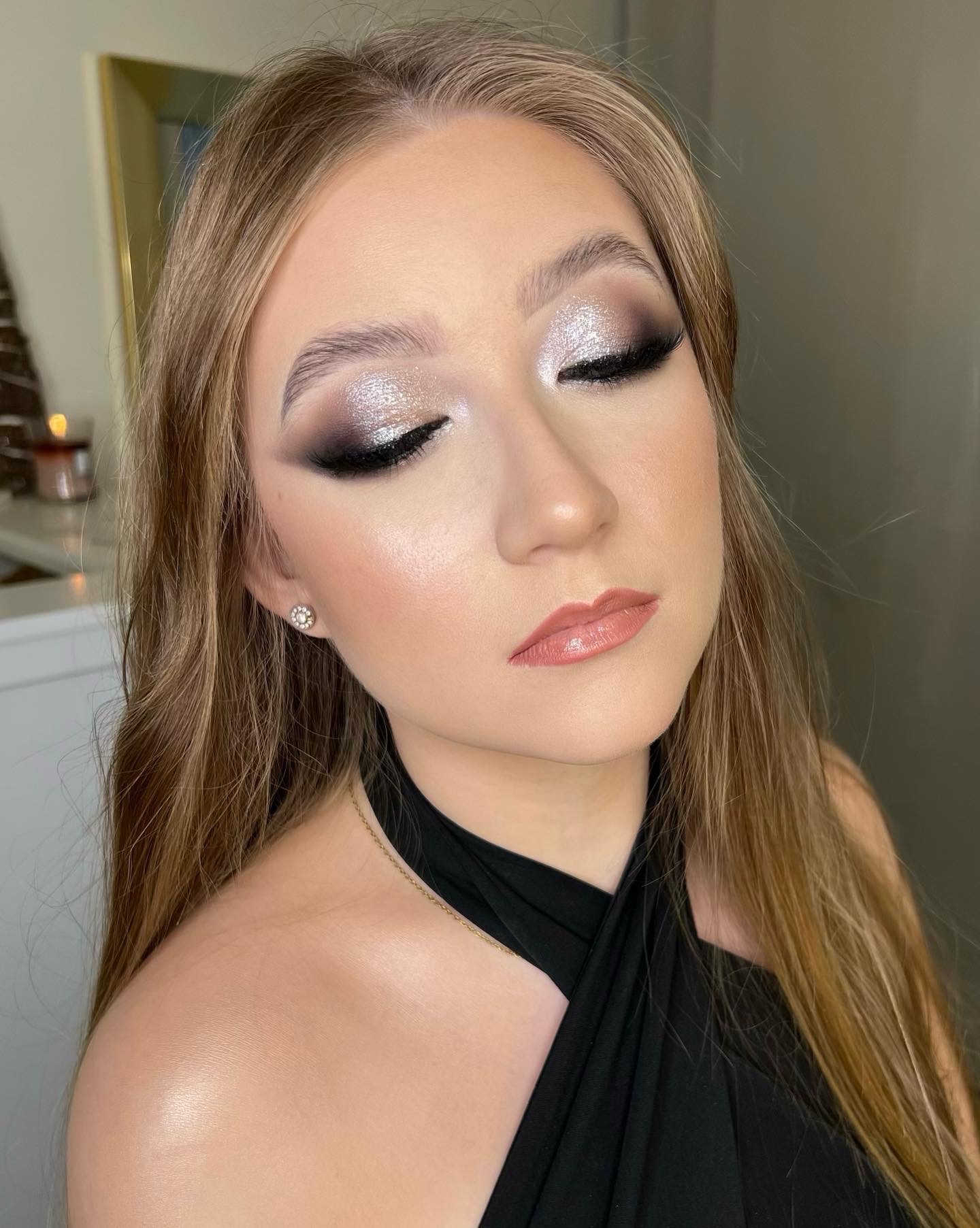 Portret kobiety z zamkniętymi oczami, prezentujący srebrzysty cień na powiekach, subtelny kontur oka i błyszczące usta w odcieniu nude, z delikatnym rozświetleniem na policzkach i małym kolczykiem...