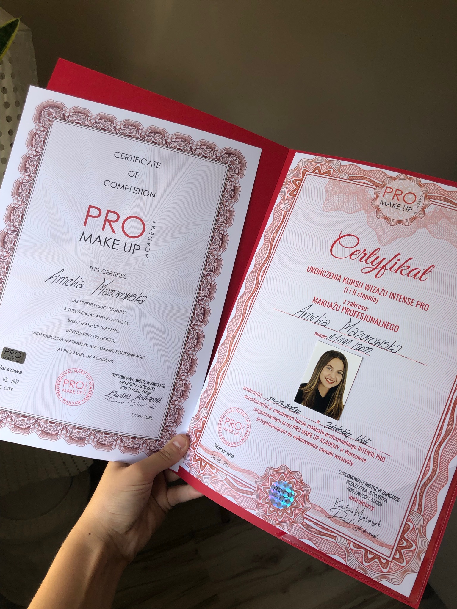 Dwa certyfikaty ukończenia kursu wizażu Intense Pro od Pro Make Up Academy, jeden w języku angielskim, drugi w języku polskim, trzymane w dłoni.