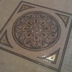 Dekoracyjna mozaika podłogowa w odcieniach beżu i brązu, z geometrycznym wzorem rozetowym w centrum kwadratowej ramy.