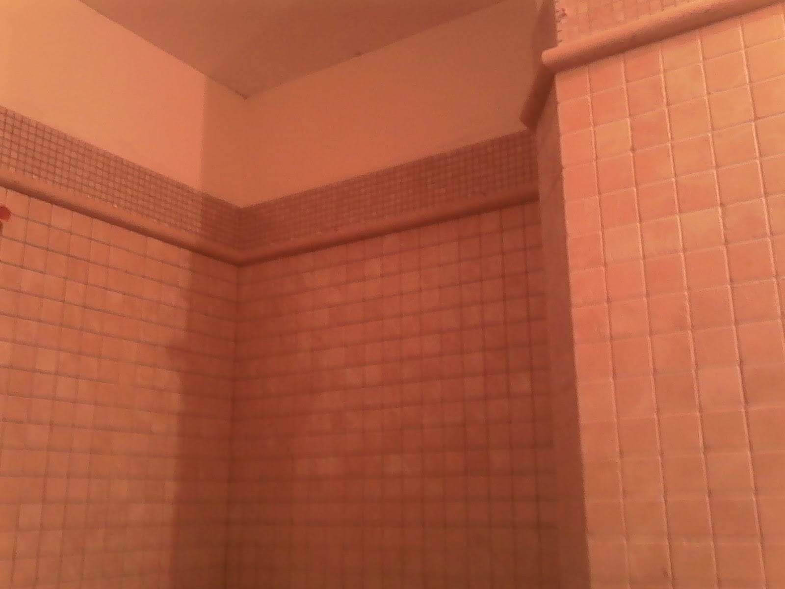 Fragment ściany i narożnika w łazience, wyłożone kwadratowymi płytkami w odcieniach brzoskwini z dekoracyjnym pasem mozaiki u góry. Widoczna góra ściany pomalowana na jasny odcień brzoskwini.