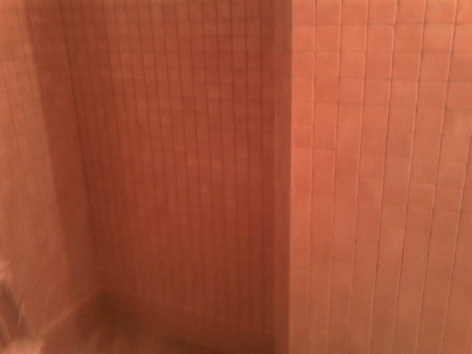 Fragment ściany wyłożonej drobną, pomarańczową mozaiką w łazience, widoczne załamanie na rogu ściany.